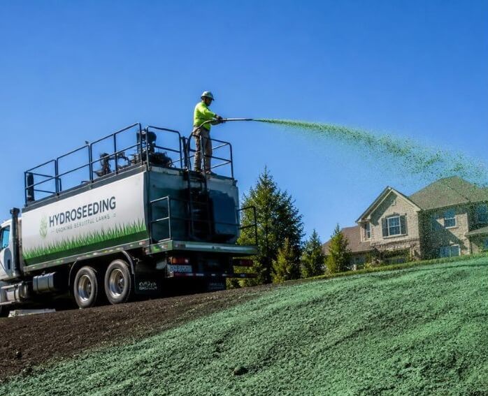 Commercial hydroseeding truck spraying green mulch slurry on a new residential lawn in Canton TX
